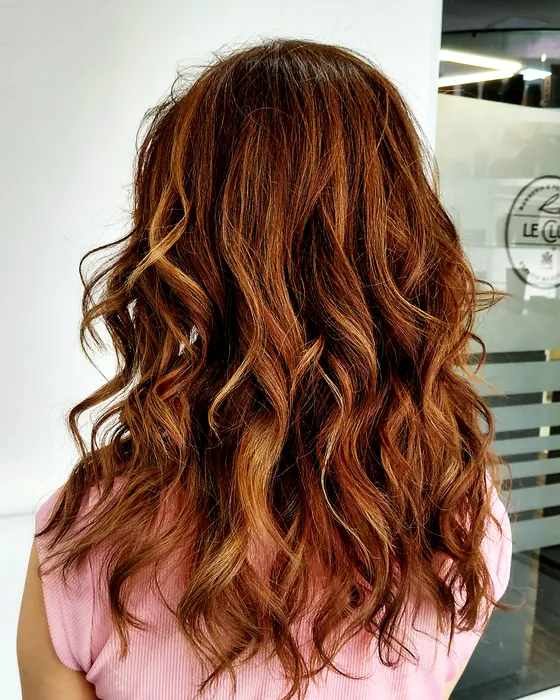 Cabello largo de tono cobrizo con mechones luminosos y acabado con ondas